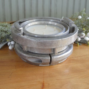 May include: A silver metal candle holder with a circular design. The holder is made of two pieces that fit together. The candle holder is sitting on a wooden surface.