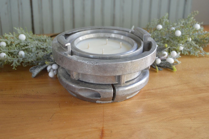 May include: A silver metal candle holder with a circular design. The holder is made of two pieces that fit together. The candle holder is sitting on a wooden surface.