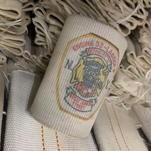 May include: A white fire hose with a red and yellow patch that says "Engine 33 Ladder Co. New York City" in a black font.