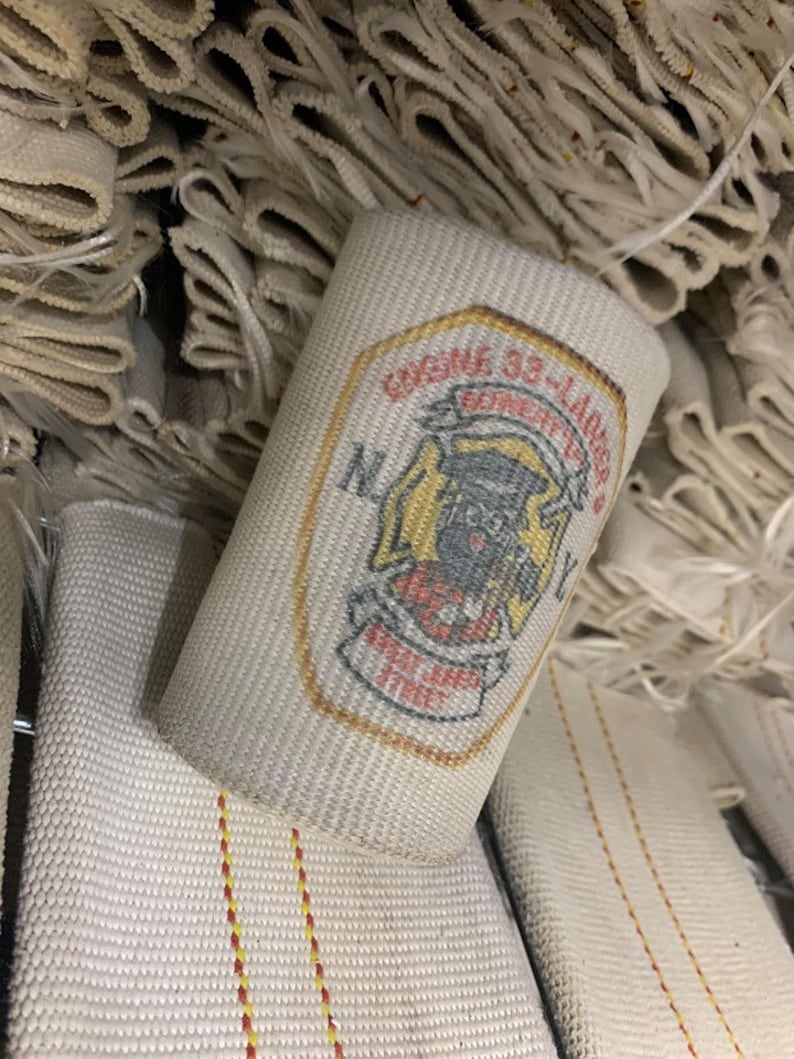 May include: A white fire hose with a red and yellow patch that says "Engine 33 Ladder Co. New York City" in a black font.