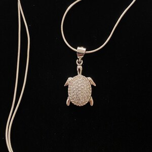 May include: A silver chain necklace with a silver turtle pendant encrusted with clear cubic zirconia stones.