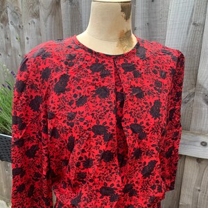 May include: A red dress with a black floral print. The dress has a round neckline and long sleeves.