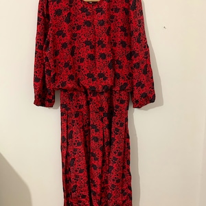 May include: A red midi dress with a black floral print. The dress has a round neckline and 3/4 sleeves.