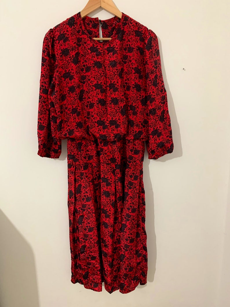 May include: A red midi dress with a black floral print. The dress has a round neckline and 3/4 sleeves.