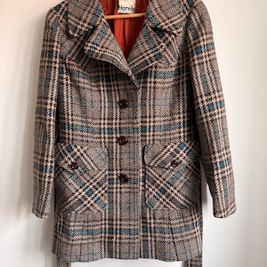 May include: A long-sleeved coat featuring a brown, beige, and teal plaid pattern. The coat has a wide collar, three dark brown buttons down the front, and two front pockets with flaps. The interior lining is a solid burnt orange color with a Harella label.