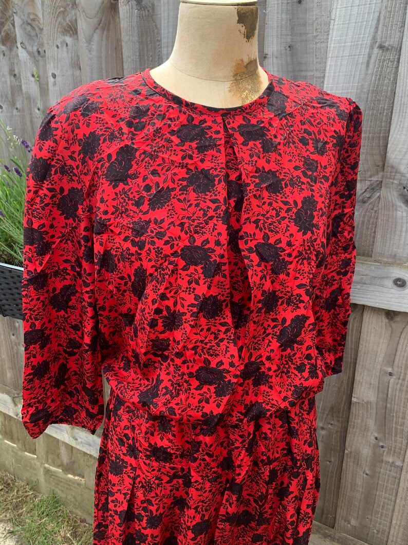 May include: A red dress with a black floral print. The dress has a round neckline and long sleeves.