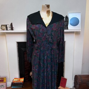 May include: A long-sleeved dress with a paisley print in shades of green, purple, and pink. The dress has a black collar and button closure.