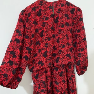 May include: A red dress with a black floral print. The dress has long sleeves and a gathered waist.
