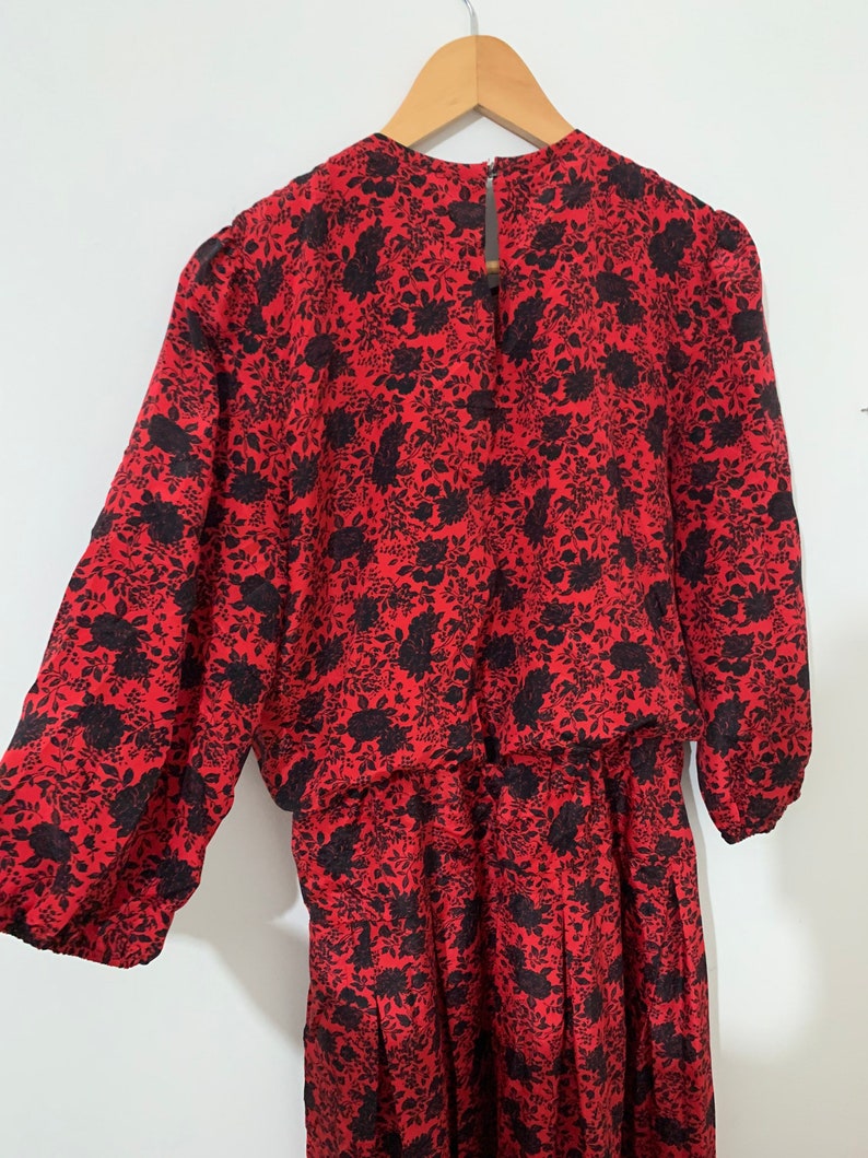 May include: A red dress with a black floral print. The dress has long sleeves and a gathered waist.