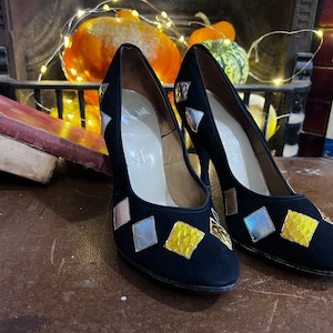 May include: Black suede high heels with diamond-shaped gold, silver, and iridescent embellishments. The shoes have pointed toes and stiletto heels, showcasing a vintage style. A classic design.