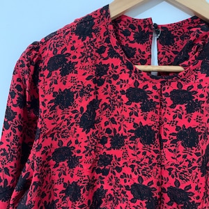 May include: A red blouse with a black floral print. The blouse has a round neckline and long sleeves.