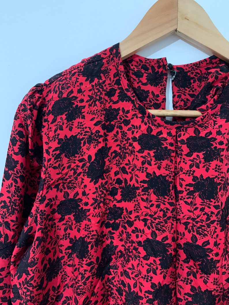 May include: A red blouse with a black floral print. The blouse has a round neckline and long sleeves.