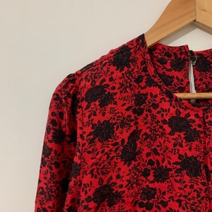 May include: A red and black floral print dress with a round neckline and long sleeves. The dress is hanging on a wooden hanger.