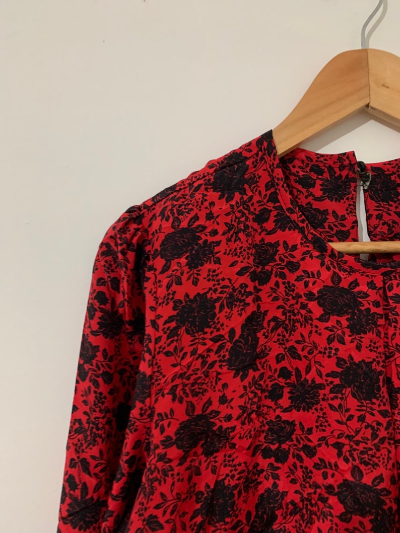 May include: A red and black floral print dress with a round neckline and long sleeves. The dress is hanging on a wooden hanger.