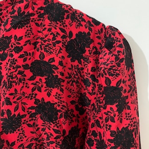 May include: Red blouse with a black floral print. The blouse has a round neckline and puffed sleeves.