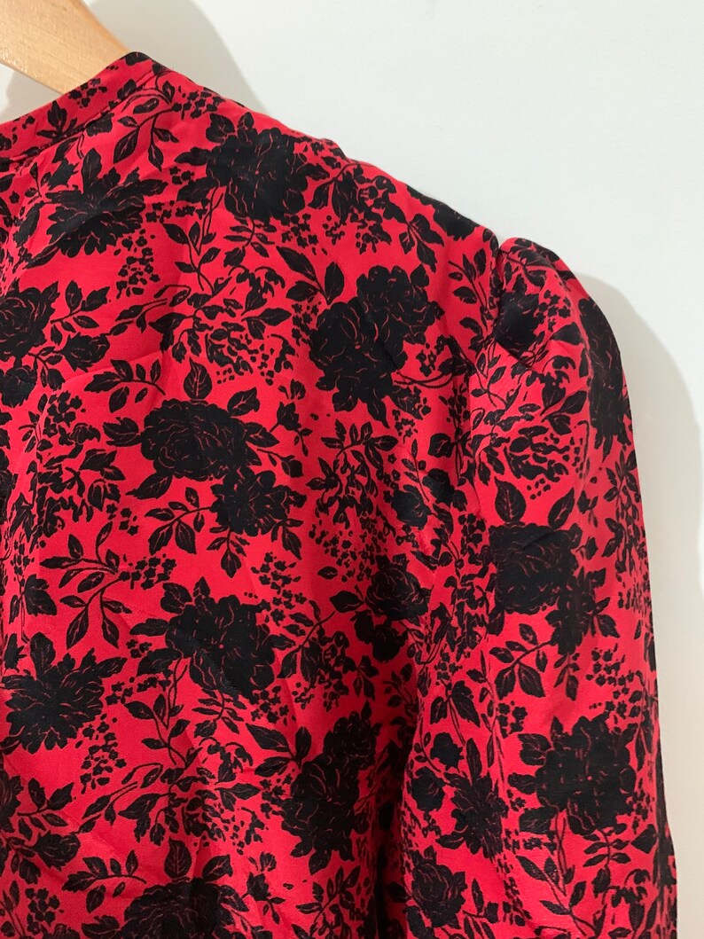 May include: Red blouse with a black floral print. The blouse has a round neckline and puffed sleeves.
