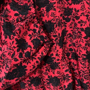 May include: Red fabric with a black floral pattern. The fabric has a gathered look and is likely a dress or skirt.