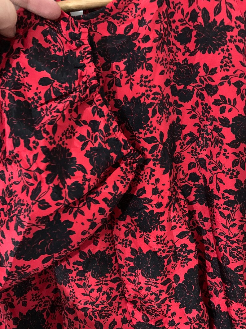 May include: Red fabric with a black floral pattern. The fabric has a gathered look and is likely a dress or skirt.