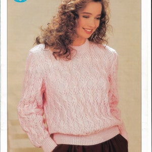 May include: A light pink knitted sweater with a textured pattern. The sweater has long sleeves and a ribbed hem and cuffs. The image also includes the Sirdar logo and the text "SIRDAR".