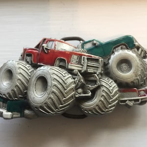 Puede incluir: Hebilla de cinturón de metal con tres monster trucks en rojo, verde y plateado. Los camiones tienen neumáticos grandes y diseños detallados. Un accesorio único para los entusiastas de los camiones.