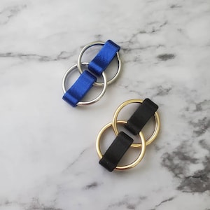 May include: Two sets of interlocking key rings. One set is silver with a blue ribbon, the other is gold with a black ribbon.