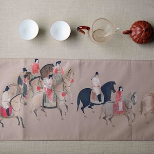 May include: A beige table runner with a traditional Chinese painting of people riding horses. The painting features a group of people in colorful clothing riding horses in a procession. The runner is perfect for adding a touch of elegance to any dining table.