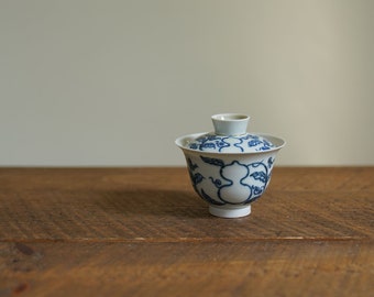 Könnte beinhalten: Eine weiße Teekanne aus Keramik mit Deckel, verziert mit einem blauen und weißen Blumendesign. Die Teekanne steht auf einer Holzoberfläche.