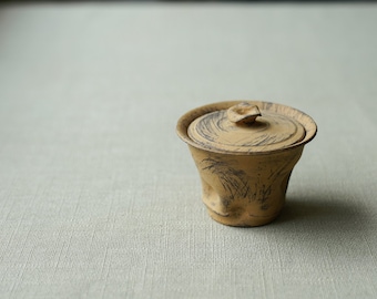 May include: A small, brown ceramic tea caddy with a lid. The caddy has a textured surface and a simple design.