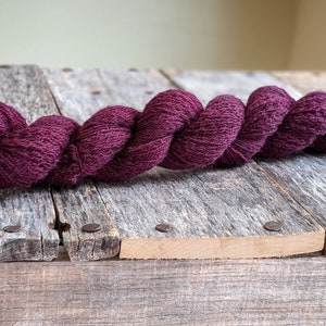 Puede incluir: Un ovillo de hilo de color morado oscuro, retorcido y enrollado, descansando sobre una superficie de madera desgastada.