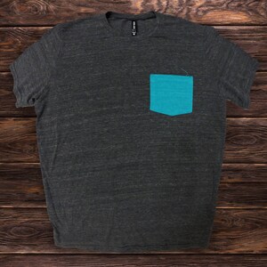 May include: A dark gray t-shirt with a teal blue pocket on the left side.