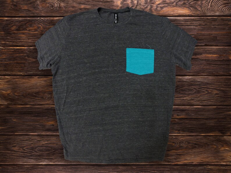 May include: A dark gray t-shirt with a teal blue pocket on the left side.