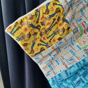 Puede incluir: Una almohada de tela blanca con un dise&ntilde;o de patchwork que presenta una tela amarilla con un patr&oacute;n repetido de Woody y Buzz Lightyear, personajes de la franquicia Toy Story. Los otros paneles de tela presentan un patr&oacute;n azul y blanco con los nombres de los personajes de la franquicia Toy Story.