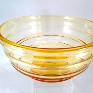 May include: A clear glass bowl with a yellow rim and decorative orange and yellow stripes. The bowl has a rounded shape with horizontal ridges. The bowl is likely vintage or antique.
