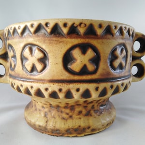 May include: A ceramic planter with two handles and a geometric design. The planter is brown and beige with a textured surface.