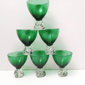 May include: Six green glass goblets are stacked in a pyramid. Each goblet has a vibrant green bowl and a clear, textured stem. These glasses are likely for serving drinks, and are a stylish addition.