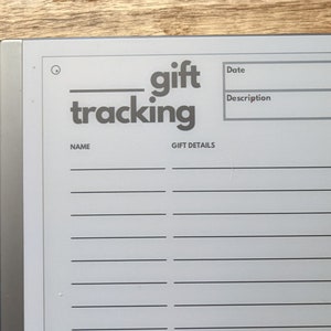 K&ouml;nnte beinhalten: Ein grauer Geschenks-Tracking-Notizblock mit einem schwarzen und silbernen Ordner. Der Notizblock hat einen Bereich f&uuml;r den Namen, das Datum, die Beschreibung, die Geschenkdetails und eine Spalte "erledigt" mit Kontrollk&auml;stchen.