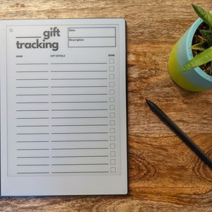 K&ouml;nnte beinhalten: Ein grauer E-Reader mit schwarzem Rand und einem Stift. Der Bildschirm zeigt eine Geschenk-Tracking-Liste mit den Worten "gift tracking" oben an. Die Liste hat Spalten f&uuml;r Name, Datum, Beschreibung und erledigt.