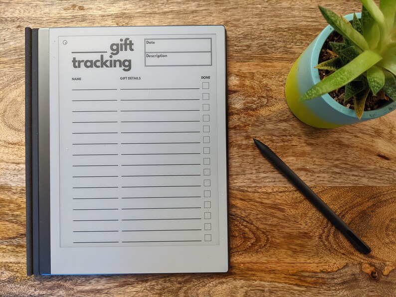 K&ouml;nnte beinhalten: Ein grauer E-Reader mit schwarzem Rand und einem Stift. Der Bildschirm zeigt eine Geschenk-Tracking-Liste mit den Worten "gift tracking" oben an. Die Liste hat Spalten f&uuml;r Name, Datum, Beschreibung und erledigt.