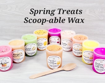 May include: A collection of ten small jars of scented wax, arranged in a semi-circle on a light wood surface. The jars are labelled with various spring-themed scents, such as "Lemon Poppy Seed Muffin", "Angel's Dessert Cake", "Cream Cheese Frosted Carrot Cupcakes", and "Strawberry Macaron & Vanilla Whip". The jars are topped with a wooden spoon.