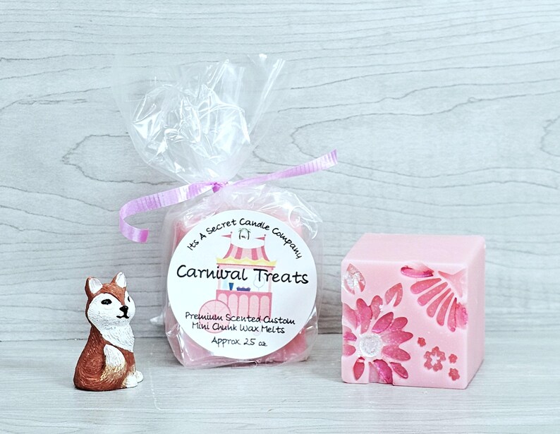 May include: A small brown and white fox figurine, a clear plastic bag containing pink wax melts with a label reading Its A Secret Candle Company Carnival Treats Premium Scented Custom Mini Chunk Wax Melts Approx 25 oz, and a pink wax cube.