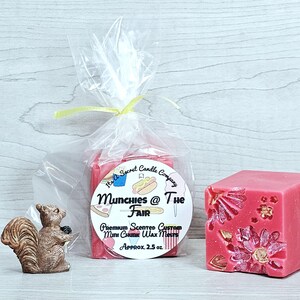 May include: A clear plastic bag containing pink wax melts with a label reading Munchies @ The Fair, Premium Scented Custom Mini Chunk Wax Melts, Approx. 71g. Next to it is a pink wax cube with floral indentations and a small brown squirrel figurine.
