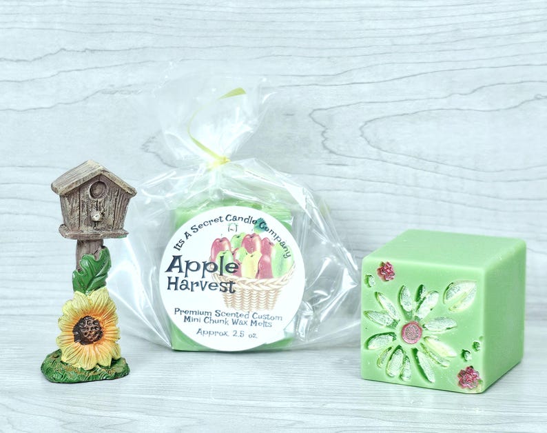 May include: A birdhouse figurine with a sunflower base, a clear plastic bag containing Apple Harvest scented wax melts with a label, and a light green cube-shaped wax melt featuring a floral pattern with pink and white accents.