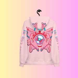 May include: A light pink hoodie with a large, colorful butterfly-eye design on the back. The design features shades of pink, blue, and red. The words "BE NOT AFRAID" are printed vertically on the left sleeve.
