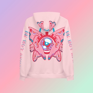May include: A light pink hoodie with a large, colorful butterfly-eye design on the back. The design features pink, blue, and orange elements. The sleeves have the text "BE NOT AFRAID" printed vertically in blue.