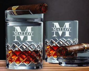 Op de afbeelding: Een set van twee gepersonaliseerde kristallen whiskyglazen met een bijpassende asbak. De glazen hebben een diamantpatroon en de asbak heeft een ingebouwde sigarenrust. De glazen zijn gegraveerd met de initialen "M" en de naam "MALLOY".