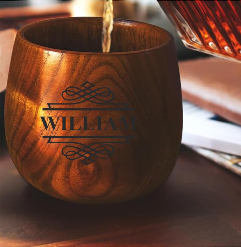 May include: A wooden cup with the name "WILLIAM" etched in black. The cup is being filled with a liquid, likely a beverage. The wood grain is visible, and the cup has a smooth, rounded shape. The overall aesthetic is rustic and elegant.
