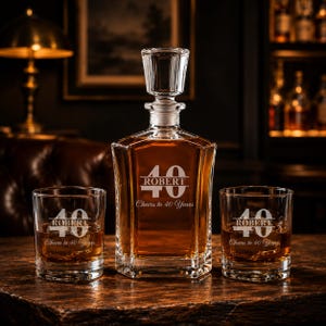 May include: A crystal decanter and two matching glasses, all engraved with "ROBERT", the number "40", and "Cheers to 40 Years". The decanter is filled with amber liquid. The set is displayed on a wooden surface.