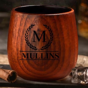 May include: A wooden tumbler with a dark brown finish. The tumbler features a black laurel wreath design with the letter "M" inside, and the name "MULLINS" below. The tumbler is designed for beverages.