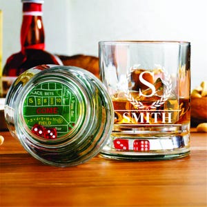 May include: Two clear glass tumblers with a green and white dice game design on the bottom. One tumbler has the name "SMITH" engraved on it with a letter "S" in a wreath design.