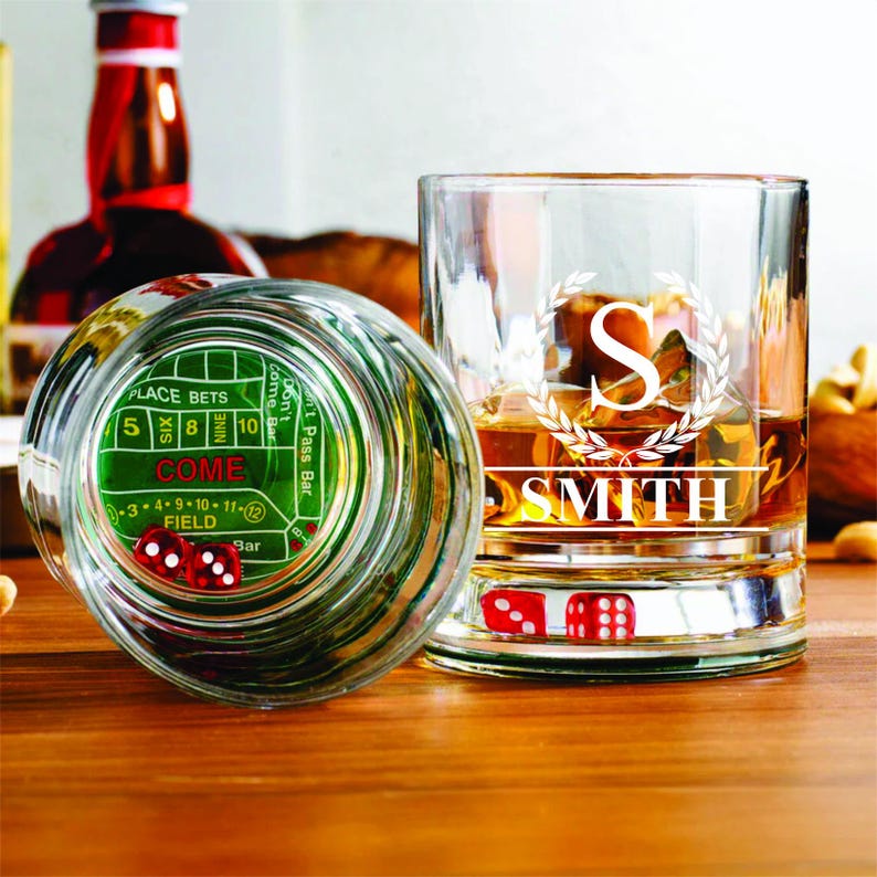 May include: Two clear glass tumblers with a green and white dice game design on the bottom. One tumbler has the name "SMITH" engraved on it with a letter "S" in a wreath design.